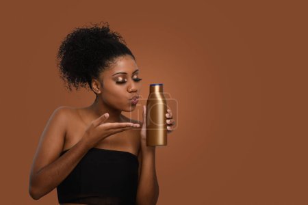 Foto de Una mujer besa una botella sin etiquetar de crema hidratante demostrando el cuidado de la piel, aislado en un fondo marrón - Imagen libre de derechos