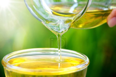 Photo for Pouring olive oil in the a glass bowl at stone kitchen and inside green garden view. Prepare for cooking concept. Healthcare and Beauty Concept. - Royalty Free Image