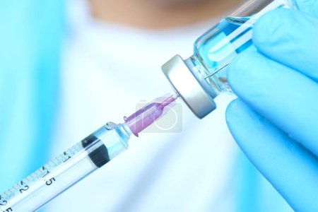 la mano del médico sostiene una jeringa y un frasco de vacuna azul en el hospital. Conceptos médicos y de salud
