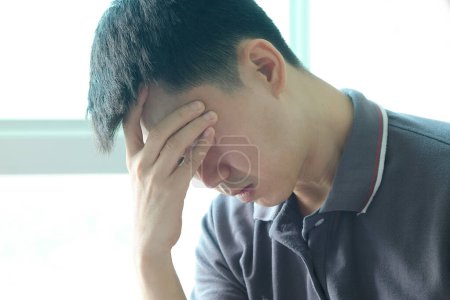 Mann, der sich hinsetzt, sein Gesicht unruhig. Am Computertisch hat sie Kopfschmerzen und Stress. Ursache harter Arbeit und unzureichender Erholung.