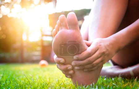 Fußschmerzen Bein einer Frau sitzt auf Gras im Park hält seine Füße und dehnt die Muskeln in der Morgensonne .Gesundheitsfürsorge und Wellness-Konzept.