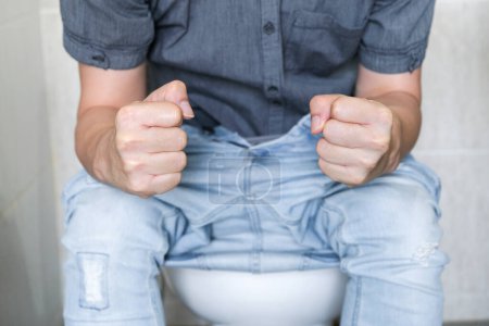 Un homme assis dans la cuvette des toilettes. Dans la salle de bain, sa maison est malheureuse avec la constipation, la diarrhée, l'intoxication alimentaire, la santé et les concepts médicaux.