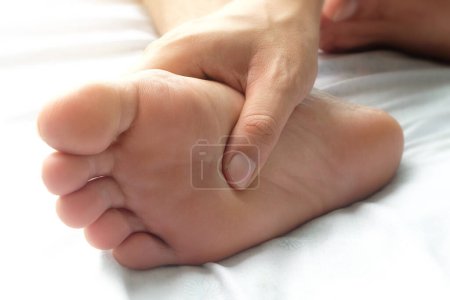 Fußschmerzen Bein der im Zimmer sitzenden Frau hält seine Füße und dehnt die Muskeln in der Morgensonne .Gesundheitsfürsorge und Wellness-Konzept.