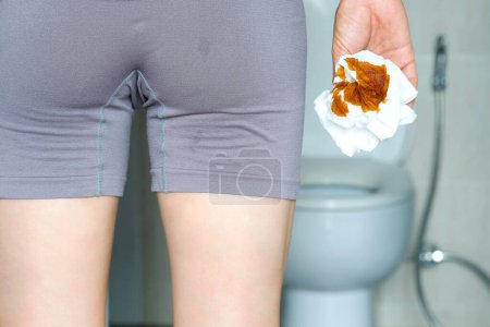The concept of constipation. The man's hand is holding a toilet paper. Stained Toilet bathroom background