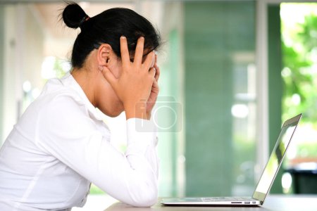 woman sitting down, his face unsettled. At the computer desk she has headaches and stress. Cause of hard work and insufficient rest.