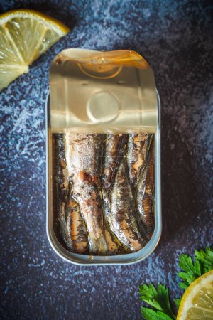 Canned sardines with olive oil open on a dark blue table with lemon and parsley. Ready for eat. 