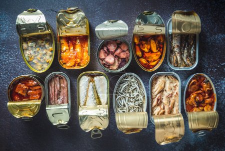 Preserve cans with different products, fish and seafood, natural or pickled, open on a dark table. Ready to eat.