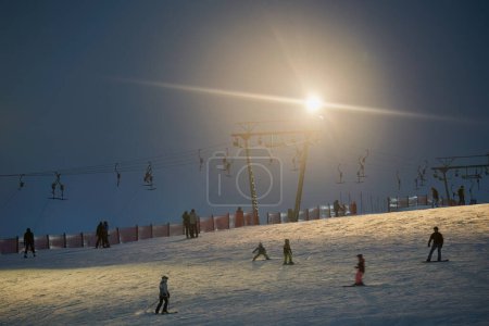 Téléchargez les photos : Treffelhausen, Germany - January 28, 2022: Ski drag lift in operation at night with lighting. Winter athletes on the slopes in the snow. Men and women active in winter sports. Long exposure, blurred. - en image libre de droit