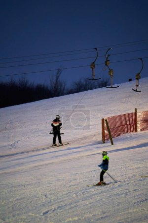 Téléchargez les photos : Treffelhausen, Germany - January 28, 2022: Ski drag lift in operation at night with lighting. Winter athletes on the slopes in the snow. Long exposure, blurred. - en image libre de droit