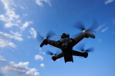 Photo for Nurtingen, Germany - June 26, 2021: Black dji fpv drone hovering in front of a blue sky. Racing drone with dark propellers and red lights. View Oblique from the lower right side. - Royalty Free Image