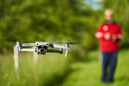 Téléchargez les photos : Nurtingen, Allemagne - 29 mai 2021 : Le drone Dji air 2s. Le système d'aéronefs sans pilote gris flotte au-dessus d'une prairie verte. Pilote hors foyer en arrière-plan. Vue de face. - en image libre de droit