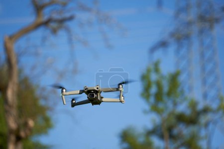 Téléchargez les photos : Nurtingen, Allemagne - 29 mai 2021 : Drone dji air 2s. Le multicopteur gris avec beaucoup de caractéristiques de sécurité offre une bonne qualité de photo et de vidéo. Arbres et poteau de puissance en arrière-plan. - en image libre de droit