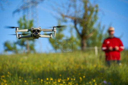 Téléchargez les photos : Nurtingen, Allemagne - 29 mai 2021 : Drone dji air 2s. Multicopter moderne sur champ de fleurs sauvages. Pilote avec pull rouge flou en arrière-plan. - en image libre de droit