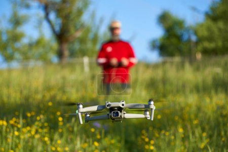 Téléchargez les photos : Nurtingen, Allemagne - 29 mai 2021 : Drone dji air 2s survole un champ de fleurs sauvages. Pilote flou avec veste rouge contrôle le système d'aéronef sans pilote. Vue de face. - en image libre de droit