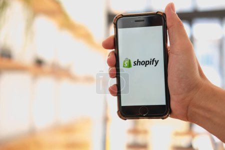 CHIANG MAI, THAILAND - 13. JANUAR 2023: Eine Frau hält ihr iPhone 8 plus Handy mit Shopify-Applikation auf dem Bildschirm in Bäckerei und Café. Shopify ist eine E-Commerce-Plattform für Online-Shops.