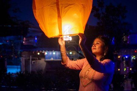 Téléchargez les photos : Fille indienne célébrant diwali en libérant lanterne ciel dans le ciel dans le cadre d'un rituel pour conjurer la mauvaise énergie. - en image libre de droit