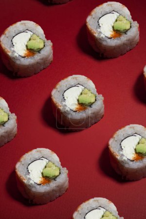 Foto de Patrón de rollos de sushi de camarones con un aguacate verde y queso sobre un fondo rojo - Imagen libre de derechos