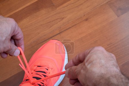 Téléchargez les photos : Mains attachant les lacets des chaussures de course orange sur un sol en bois, vue à la première personne, horizontale - en image libre de droit