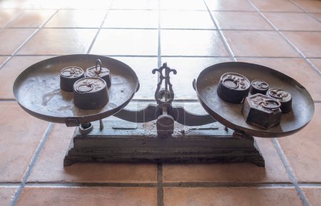 an antique scale with weights of different sizes on both sides, on a rustic floor,old weight, antique vintage balance, old scales on a tile surface, horizontal