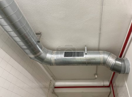 ventilation system, stainless steel pipe for air conditioning or heating distribution, together with red pipes on a white ceiling, horizontal