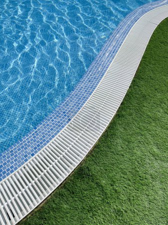 edge of an s shaped swimming pool, with crystal clear water, a white pool trellis and green grass, vertical