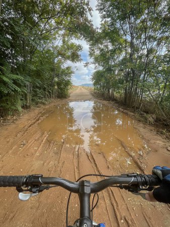 Photo for First person view of the handlebars of a mountain bike just before crossing a large puddle of mud and water on a path through a forest, vertical - Royalty Free Image