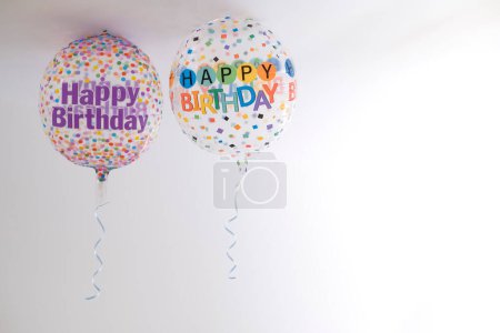 Téléchargez les photos : Deux ballons en hélium décorés de points colorés et d'un message joyeux anniversaire, avec un ruban suspendu, sur le toit d'une pièce blanche, espace de copie, fond dégradé, horizontal - en image libre de droit