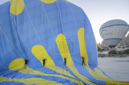 Photo for Four men deflate a blue and yellow hot air balloon, pushing the air inside it out, teamwork concept, Goreme air balloon air field, Cappadocia, Anatolia, Turkey - Royalty Free Image