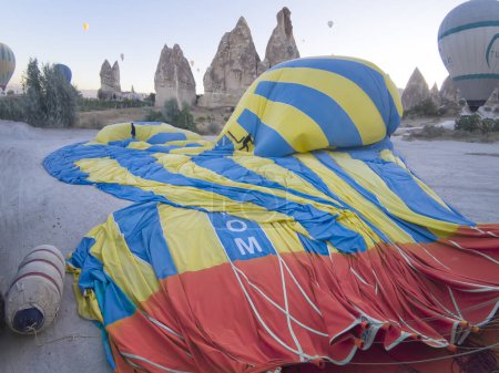 Photo for Two men deflate a blue, red and yellow hot air balloon, pushing the air inside it out, teamwork concept, rock hoodoos at the background, Goreme air balloon air field, - Royalty Free Image