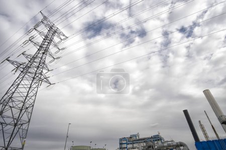 Photo for Electric grid pylon seen from below, electricity grid pole in a cloudy sky, shot from the perspective of looking up from below, high-voltage tower and some chimneys and a factory, copy space, horizontal - Royalty Free Image