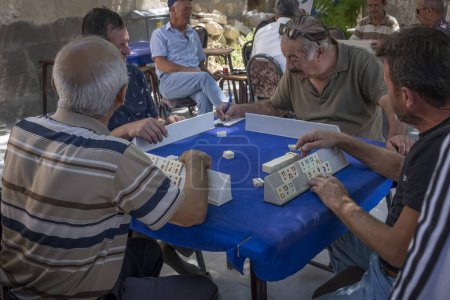 Téléchargez les photos : Un groupe de retraités turcs jouant okey à une table dans la rue, l'un d'eux écrit le résultat du jeu dans un carnet - en image libre de droit