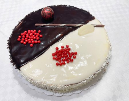 a delicious half dark chocolate, half white chocolate cake decorated with red balls and a chocolate wafer with sweet coconut shavings, horizontal