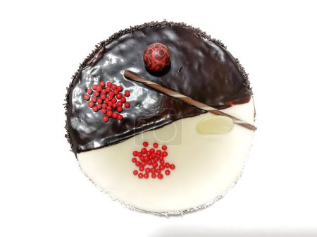 top view of a delicious half dark chocolate, half white chocolate cake decorated with red balls and a chocolate wafer with sweet coconut shavings, horizontal