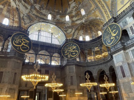 Téléchargez les photos : Trois boucliers avec des inscriptions arabes avec des noms de personnalités islamiques illustres et des lampes suspendues à l'intérieur de la mosquée de sainte sofia à Istanbul, horizontale - en image libre de droit