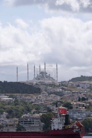 Camlica Moschee mit ihren sechs Minaretten, von einem Boot auf dem Bosporus aus gesehen, im Vordergrund ein Frachtschiff mit einem türkischen Boot und Wohngebäuden auf dem Hügel, senkrecht