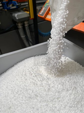 Photo for Pouring of a bag of white plastic pellets on a gray plastic drawer, production of plastic parts, plastic injection, spilling of plastic pelets, with a plastic injector out of focus in the background, small plastic granules vertical - Royalty Free Image