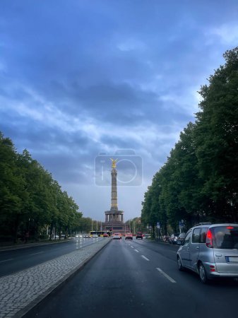 Siegessäule auf der Allee des 17. Juni in Berlin, zur blauen Stunde an einem Tag mit stürmischem Himmel, im Vordergrund ein Auto, senkrecht
