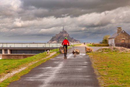 Téléchargez les photos : Un cycliste se dirige vers un barrage le long d'un canal en Normandie près de la ville d'Avranches par une journée nuageuse. France. - en image libre de droit