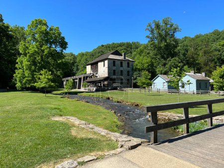 Mercantile, Apothecary, Saw Mill and Grist Mill beside a creek with a foot bridge in the recreated and restored 1800 Pioneer Village at Spring Mill State Park, near Mitchell, Indiana with beautiful blue sky copy space and vivid green trees and grass.