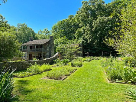 Histórica residencia superior y jardín exterior en el recreado y restaurado 1800 Pioneer Village en Spring Mill State Park, cerca de Mitchell, Indiana, con hermoso cielo azul y vívidos árboles verdes y espacio de copia de hierba.
