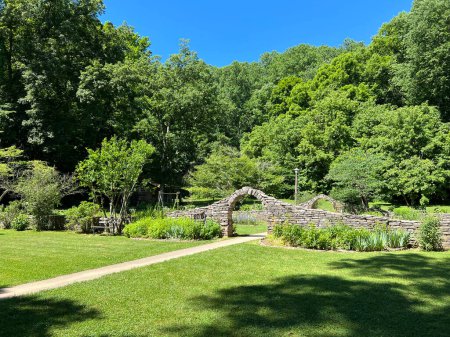 :  Entrada al jardín en el recreado y restaurado 1800 Pioneer Village en Spring Mill State Park, cerca de Mitchell, Indiana, con hermoso cielo azul y vívidos árboles verdes y espacio de copia de hierba.