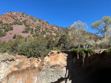 Springtime view of the red rocky mountain landscape in Tonto Natural Bridge State Park in Pine, Arizona with bright blue sky copy space in an area showing the foot bridge and the small waterfall above the natural bridge.