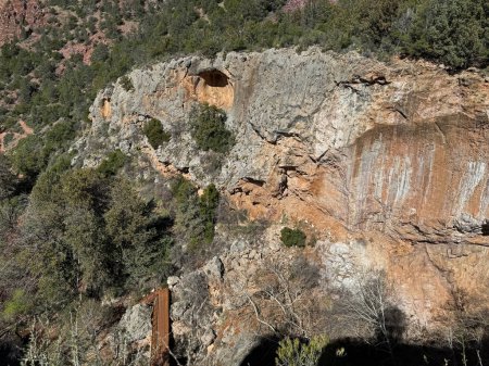 Springtime view of the white and rusty rocky cliff and walking bridge leading to the natural bridge in Tonto Natural Bridge State Park in Pine, Arizona.