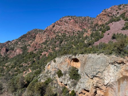 Foto de Vista primaveral del paisaje rocoso rojo de la montaña en el Parque Estatal Tonto Natural Bridge en Pine, Arizona con espacio para copiar el cielo azul brillante en un área por encima del puente natural. - Imagen libre de derechos