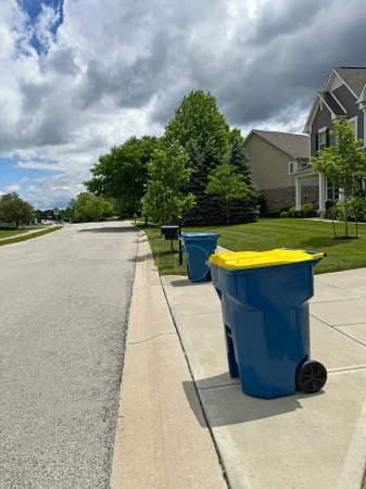 Blaue Mülltonnen, darunter ein gelber Papierkorb, neben der Straße am Abfalltag in einem Viertel von Indiana mit Kopierraum.