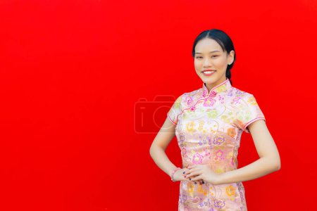 Foto de Hermosa mujer asiática con el pelo largo que lleva vestido de Cheongsam rosa en tema de año nuevo chino, mientras que ella muestra su mano como saludo chino con fondo rojo. - Imagen libre de derechos