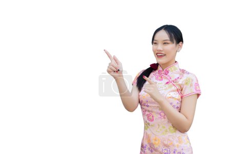 Asiatische Frau mit langen Haaren, die rosafarbenes Cheongsam-Kleid im chinesischen Neujahrsthema trägt, während sie anwesend ist und von Hand zu Hand zeigt und in die Kamera schaut, während sie einen isolierten weißen Hintergrund hat.