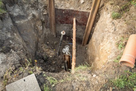 Es wurde ein Loch gegraben, um das Rohr zu reparieren und den Wasserhahn zu wechseln. Kanalgraben mit Rohren. Reparatur der unterirdischen Kommunikation. Abwasser- und Wasserleitung unter dem Boden des Grabens. Das Konzept der Reparatur von Wasserversorgung und Abwassersystemen.
