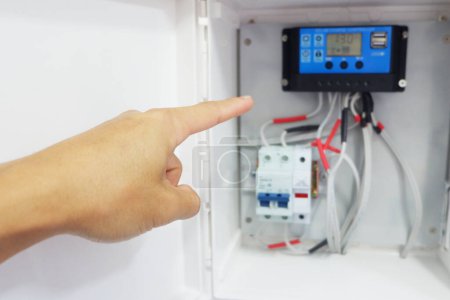 Photo for Man's hand showing the installation of a solar charger and circuit breaker in a cabinet for a solar cell system. - Royalty Free Image