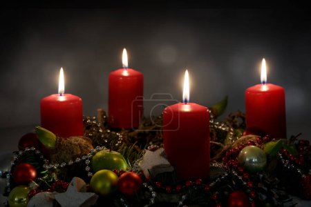 Kerzenschein in der Nacht, Teil eines Adventskranzes mit vier roten Kerzen und Weihnachtsdekoration vor dunklem Hintergrund, Kopierraum, ausgewählter Fokus, enge Schärfentiefe